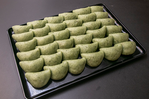 半月形によもぎで包んだ餅が盆に並ぶ